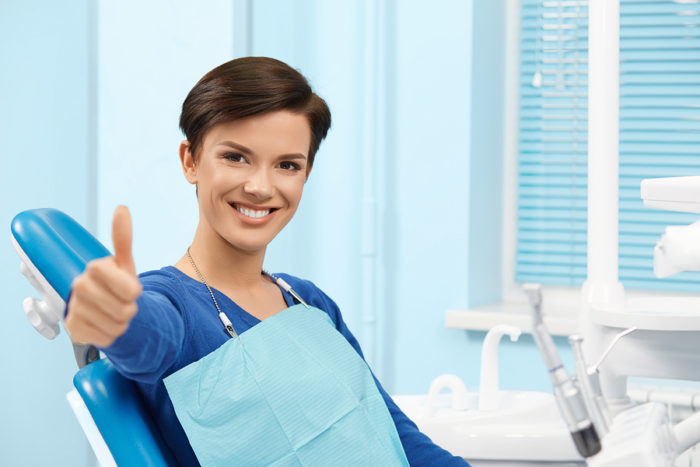 Young female patient visiting dentist office smiling and making thumbs up.