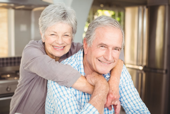 Portrait of cheerful senior couple embracing in kitchen at home